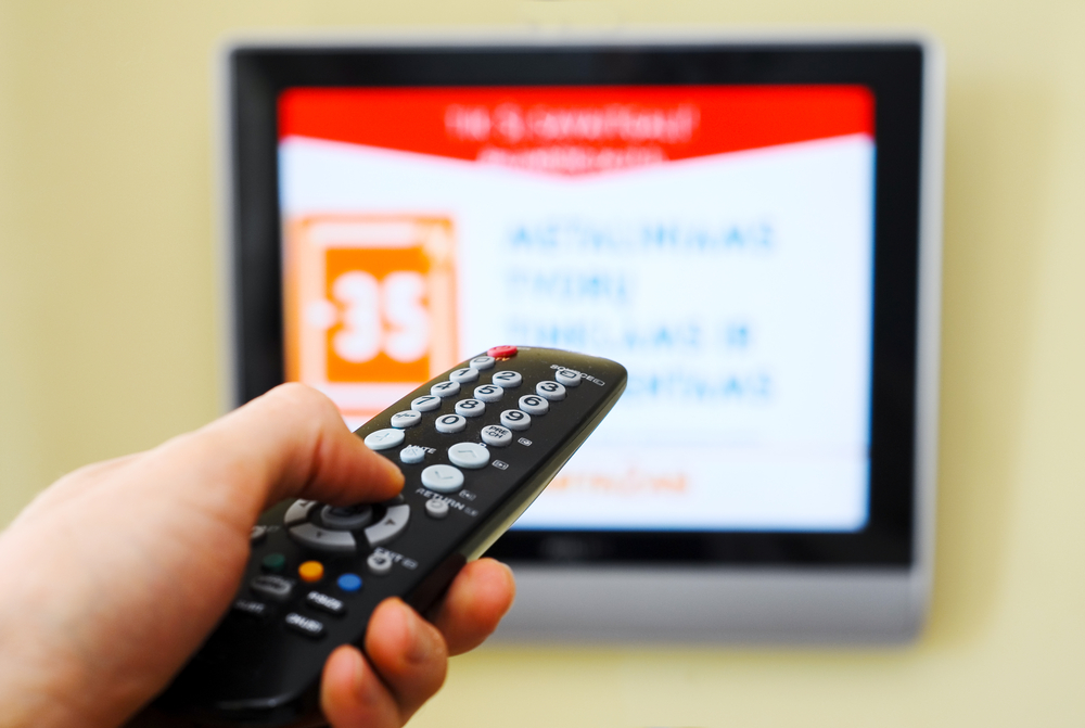a hand holds a TV remote while pointing it to a blurred TV screen